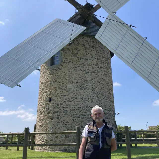 Man standing in front of a stone windmill with white blades