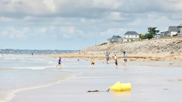 Plusieurs enfants courent sur une plage de sable avec des maisons en arrière-plan à Hauteville-sur-Mer