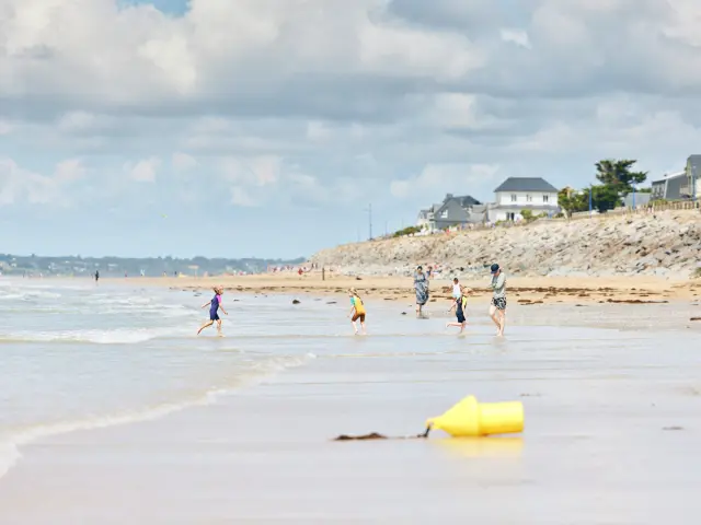 Plusieurs enfants courent sur une plage de sable avec des maisons en arrière-plan à Hauteville-sur-Mer