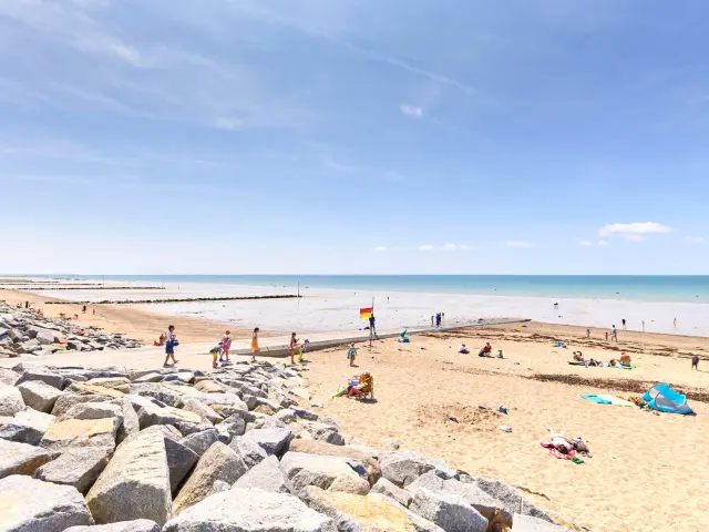 Plage avec des personnes se baignant et des parasols, bordée par l'océan