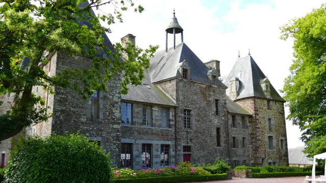 Manoir victorien en pierre avec des fenêtres éclairées, entouré de haies et d'arbres