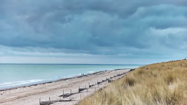 Plage de sable à Gouville-sur-Mer avec des nuages sombres au-dessus