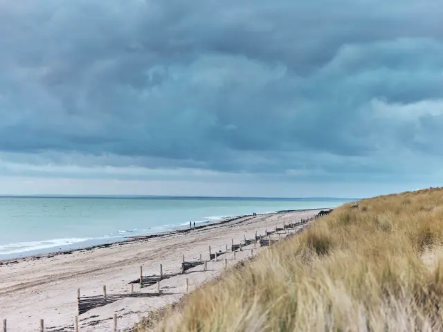 Plage de sable à Gouville-sur-Mer avec des nuages sombres au-dessus