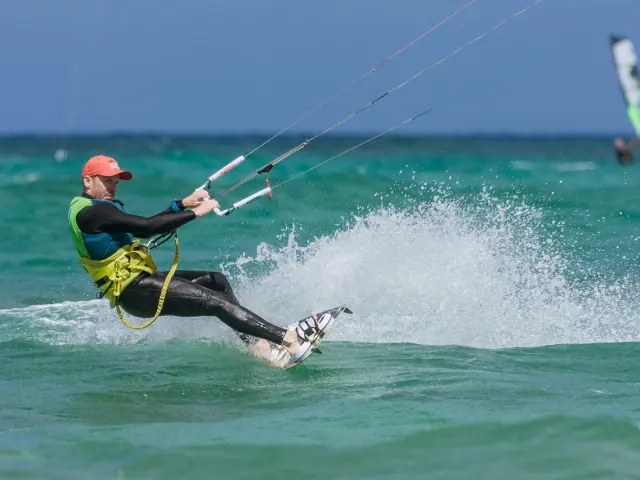 Ein Kitesurfer in einem schwarzen und gelben Neoprenanzug surft auf türkisfarbenem Wasser