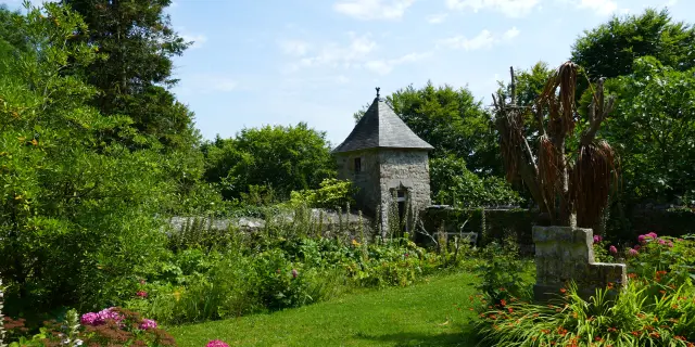 Église en pierre avec un clocher pointu entourée d'un jardin fleuri et de plantes vertes