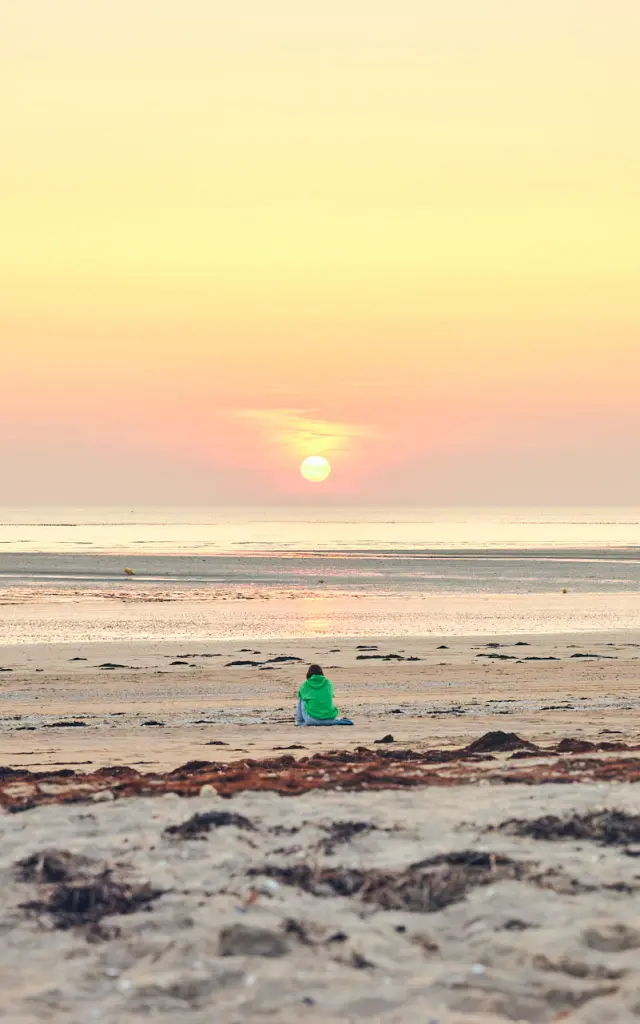 Une personne en silhouette sur une plage de Lingreville au coucher du soleil