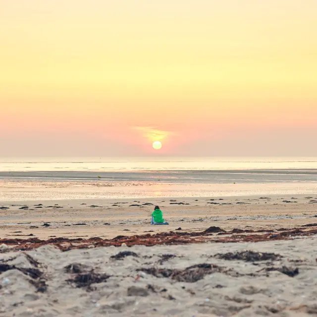 Personne debout sur la plage face à un coucher de soleil, avec des voiliers amarrés en arrière-plan