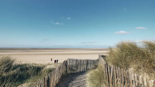 Sentier en bois menant à une plage déserte sous un ciel bleu : Montmartin sur Mer