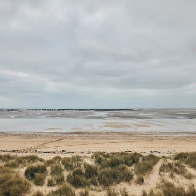 Leerer Strand mit Fußabdrücken und Wasserpfützen