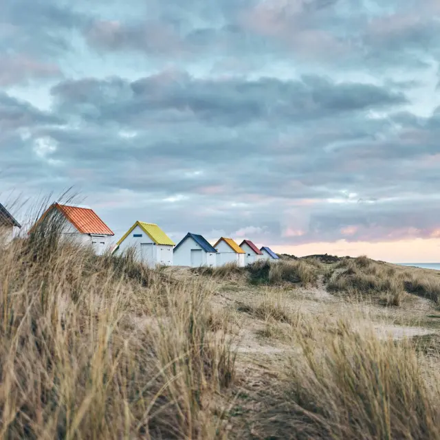 Eine Reihe bunter Strandhütten auf einer grasbewachsenen Düne in der Nähe des Meeres