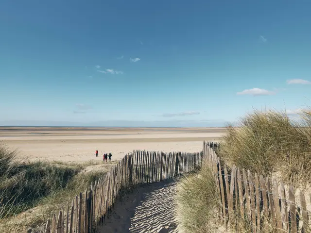 Holzweg, der zu einem einsamen Strand unter einem blauen Himmel führt