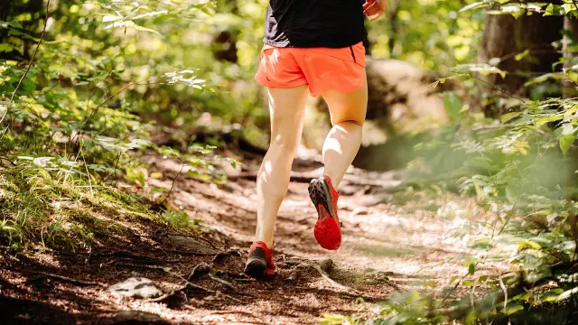 Un coureur en short orange et t-shirt noir court sur un sentier forestier