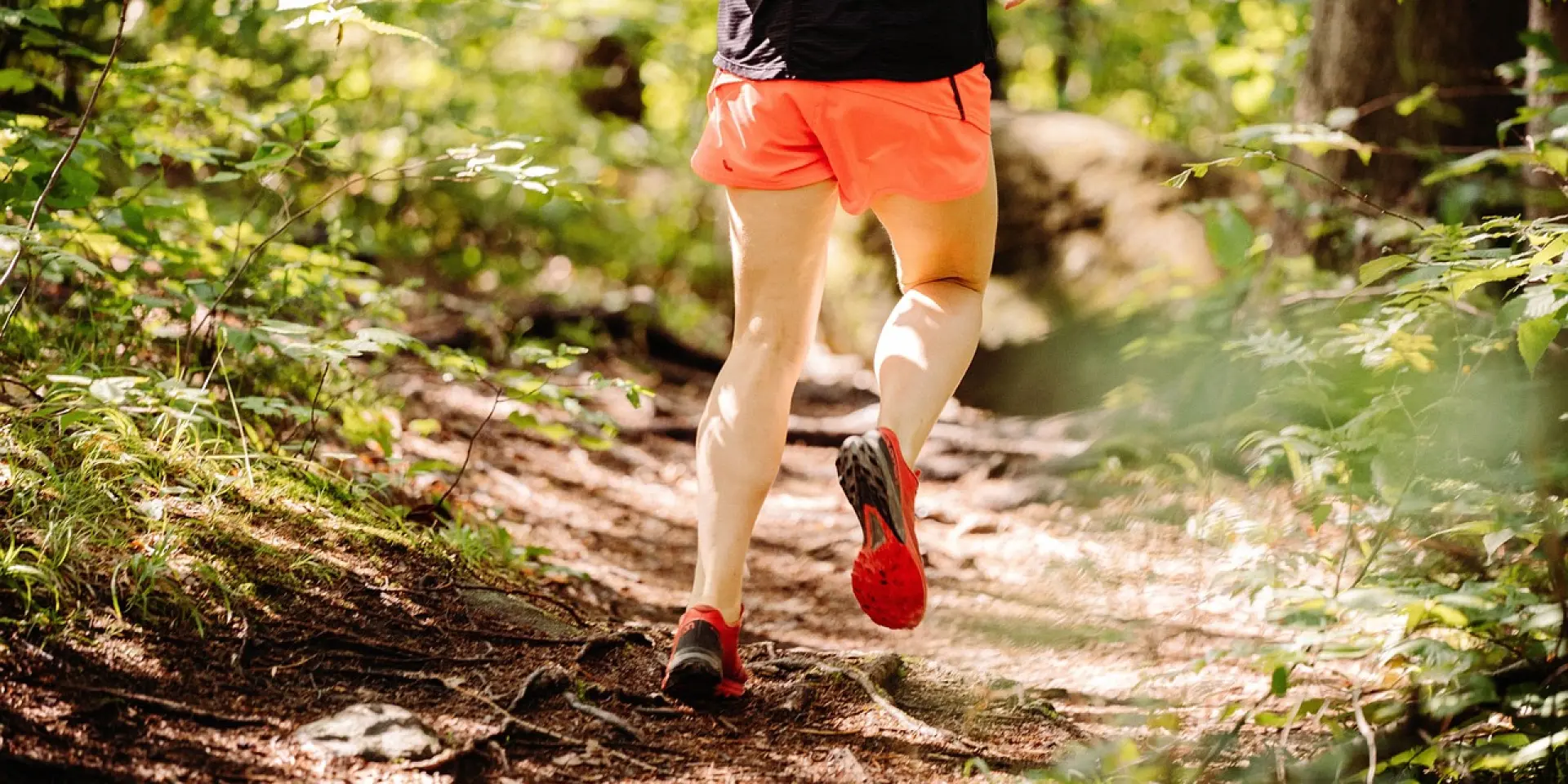 Un coureur en short orange et t-shirt noir court sur un sentier forestier