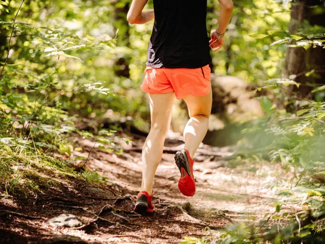 Un coureur en short orange et t-shirt noir court sur un sentier forestier