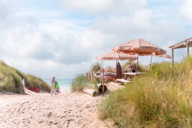 Deux personnes marchant sur une plage avec des parasols et des chaises longues - Paillotte Anneville sur Mer