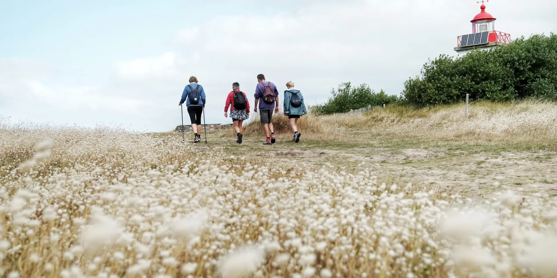 Quatre personnes marchent vers un phare sur un chemin herbeux à la pointe d'Agon
