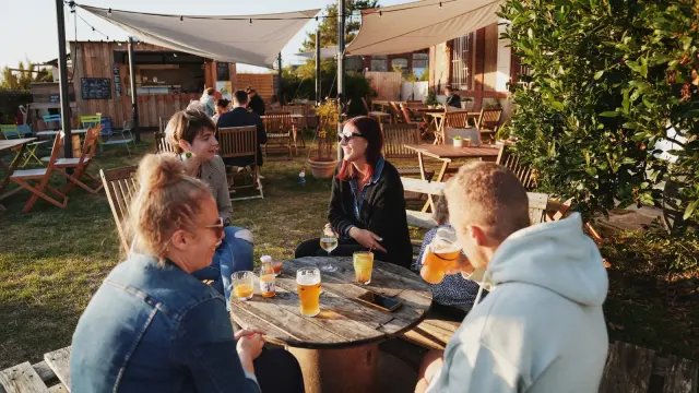 Groupe d'amis assis autour d'une table en bois en terrasse à la petite Gare de Regnéville sur Mer
