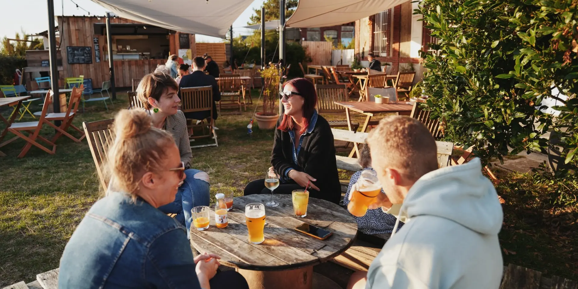 Groupe d'amis assis autour d'une table en bois en terrasse à la petite Gare de Regnéville sur Mer