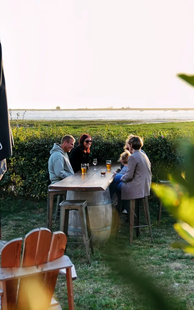 Quatre personnes dînent à une table en plein air près de l'eau : la petite Gare Regnéville sur Mer