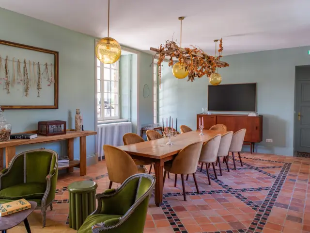 Salle à manger avec une grande table en bois, des chaises et des luminaires suspendus : eco domaine du Plessis