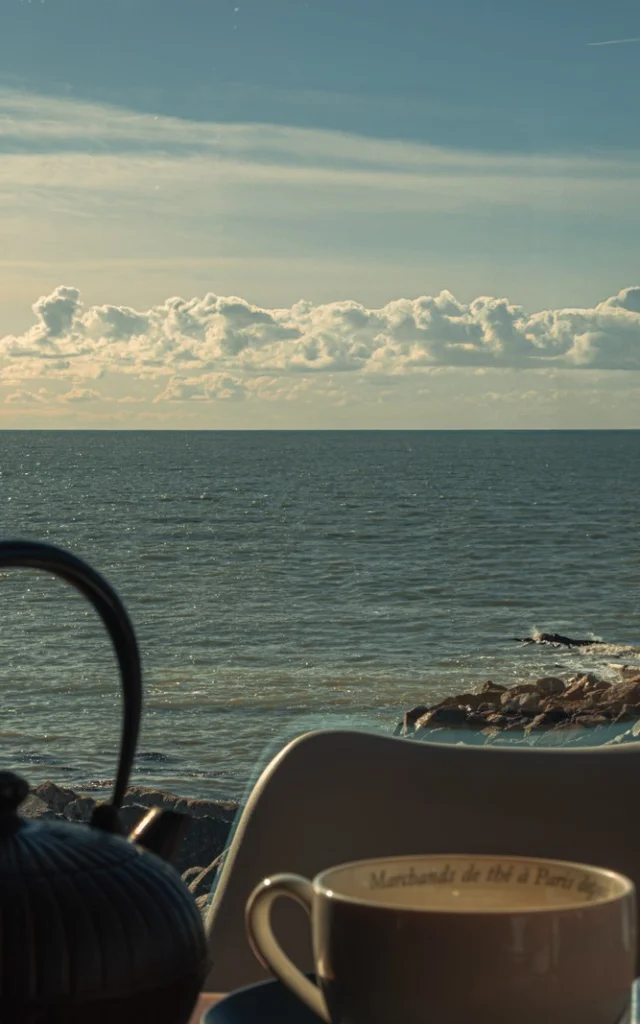 Une théière et une tasse de thé sur une table près de la mer à Agon-Coutainville
