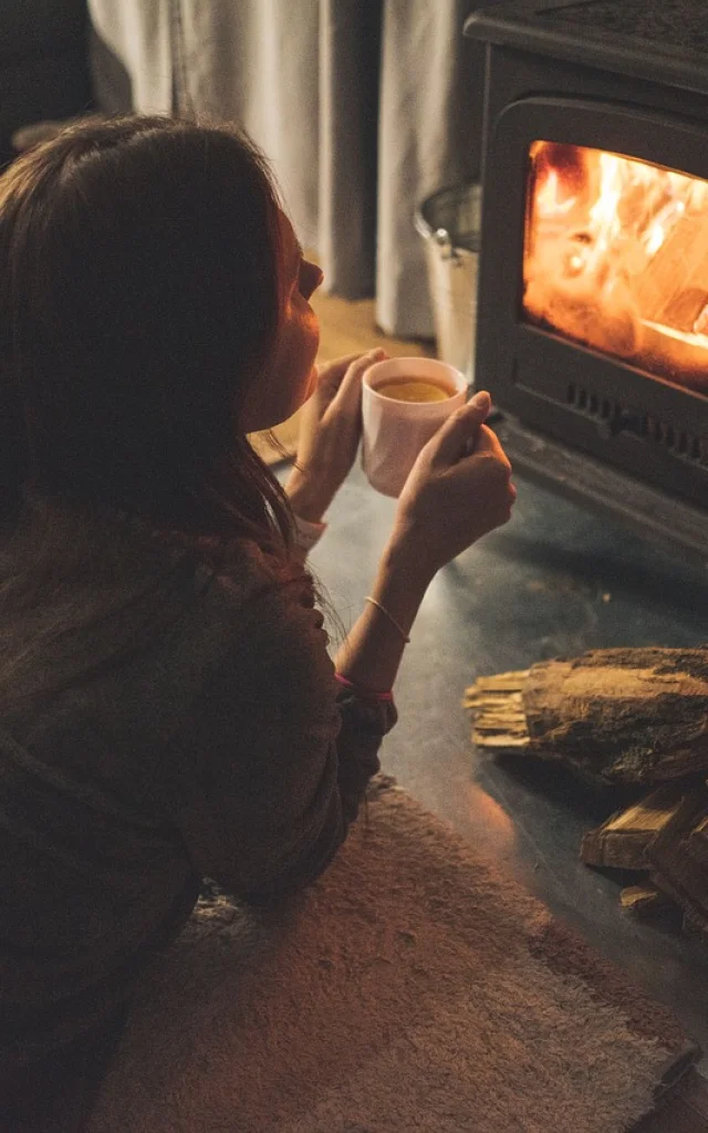 Une personne assise devant un feu de cheminée, tenant une tasse.