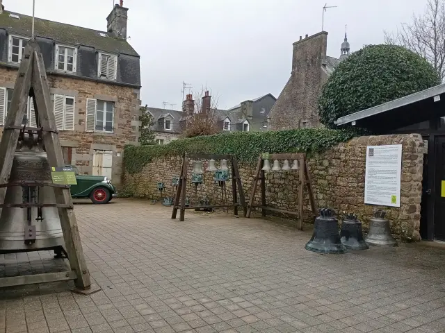 Ruelle pavée bordée de bâtiments en pierre, avec des passants sous la pluie et des volets verts