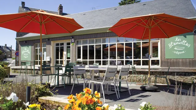 Terrasse d'un restaurant en bord de mer avec des tables et chaises sous des parasols rouges