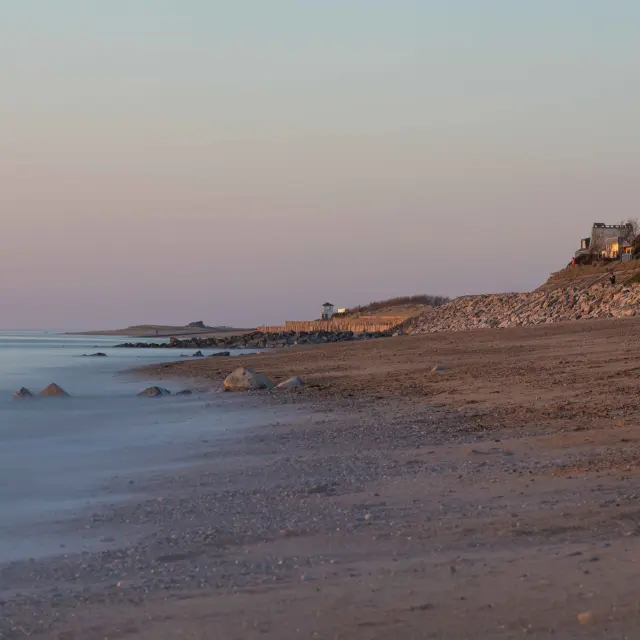 Plage avec des rochers et des bâtiments en arrière-plan au coucher du soleil