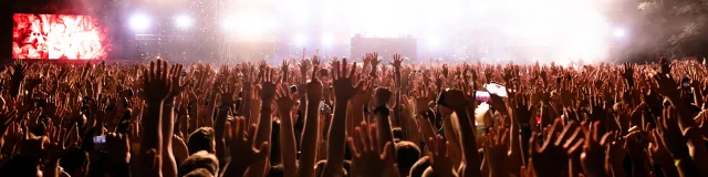Rear view of excited people with arms raised having fun while watching confetti fireworks in front of the stage at music festival. Copy space.