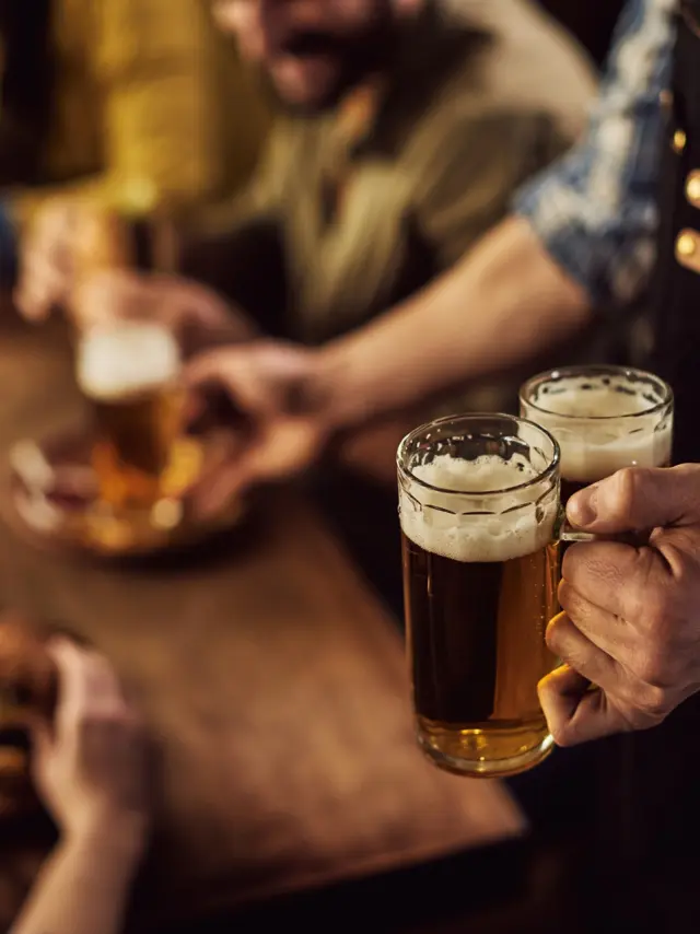 Close-up of waiter serving beer to customers in a pub.