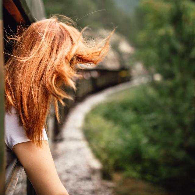 Happy smiling redhead woman looks out from window traveling by train