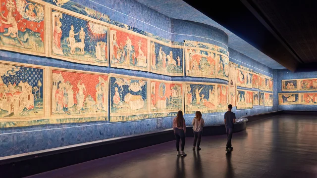 3 personnes marchant dans la galerie et observant la tapisserie
