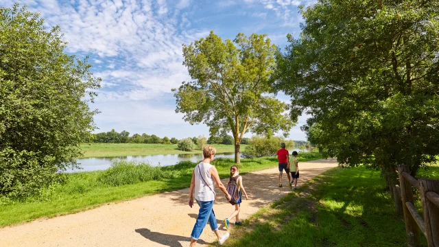 Une famille de 2 adultes et 4 enfants, de dos, marchent sur le chemin qui longe la rivière