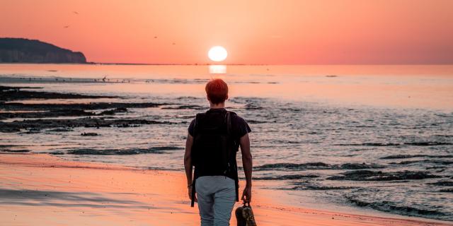 Jeune homme marchant sur la plage de Dieppe à marée basse durant le coucher de soleil