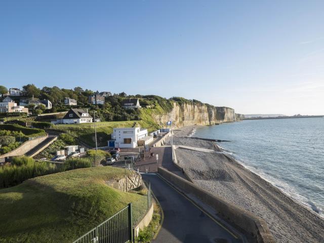 Point de vue sur la plage de Puys où l'on aperçois les falaises beiges recouvertes de vert, la plage de galets et la mer.