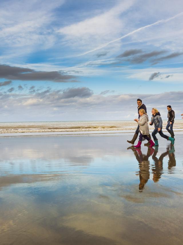Famille en bottes et tenues hivernales marchant sur la plage à marée basse