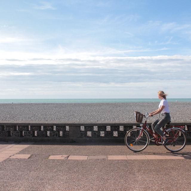 Jeune femme pédalant sur la piste cyclable du front de mer de Dieppe, galets et mer à l'horizon