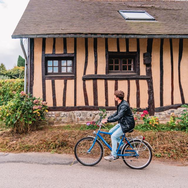 Jeune homme à vélo devant une maison à colombage dans le village de Varengeville-Sur-Mer.