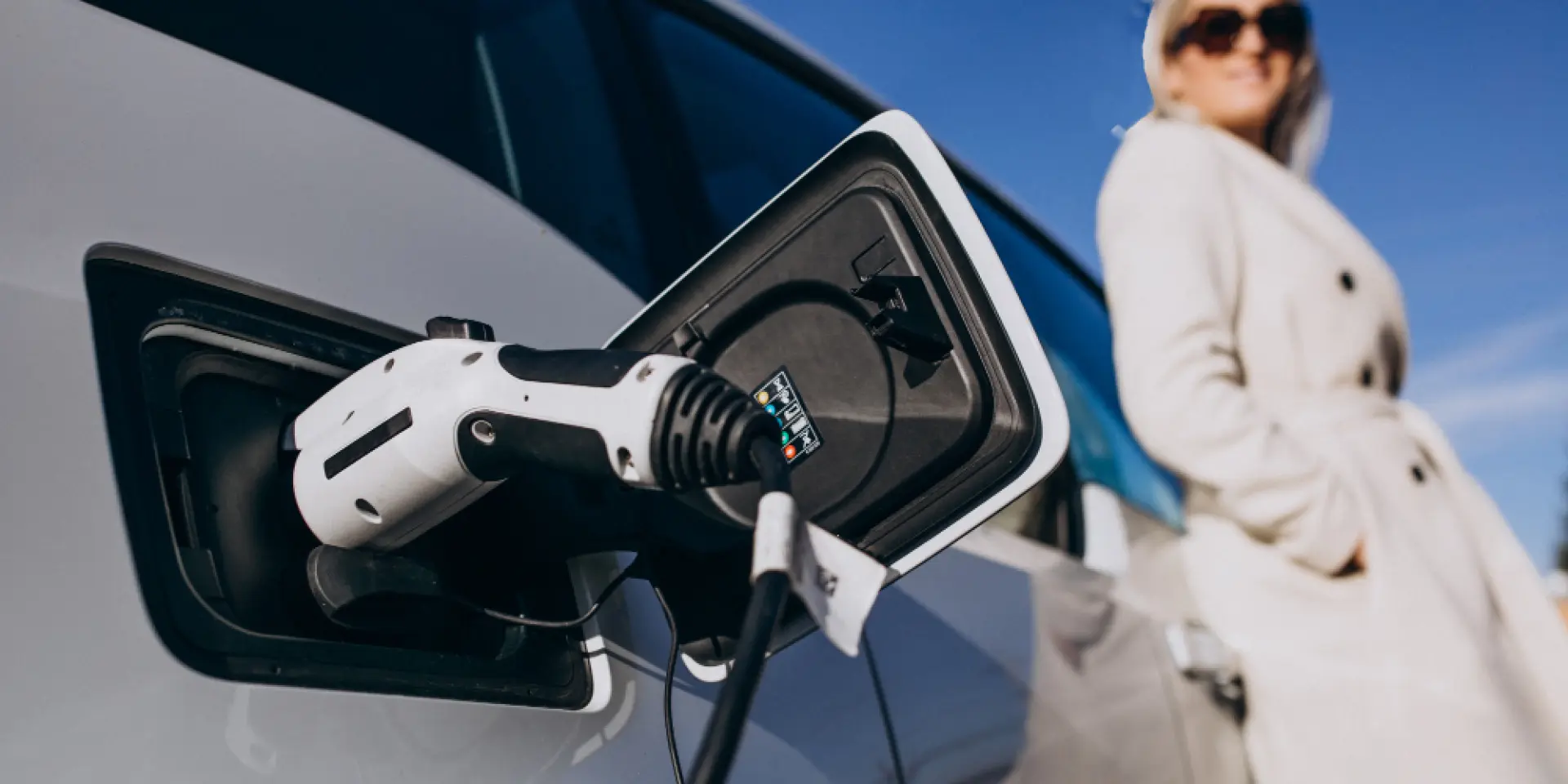Câble de recharge d'une voiture électrique blanche avec une dame regardant la voiture charger