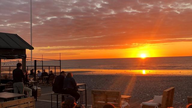 Terrasse d'un bar sur les galets devant un coucher de soleil face à la mer