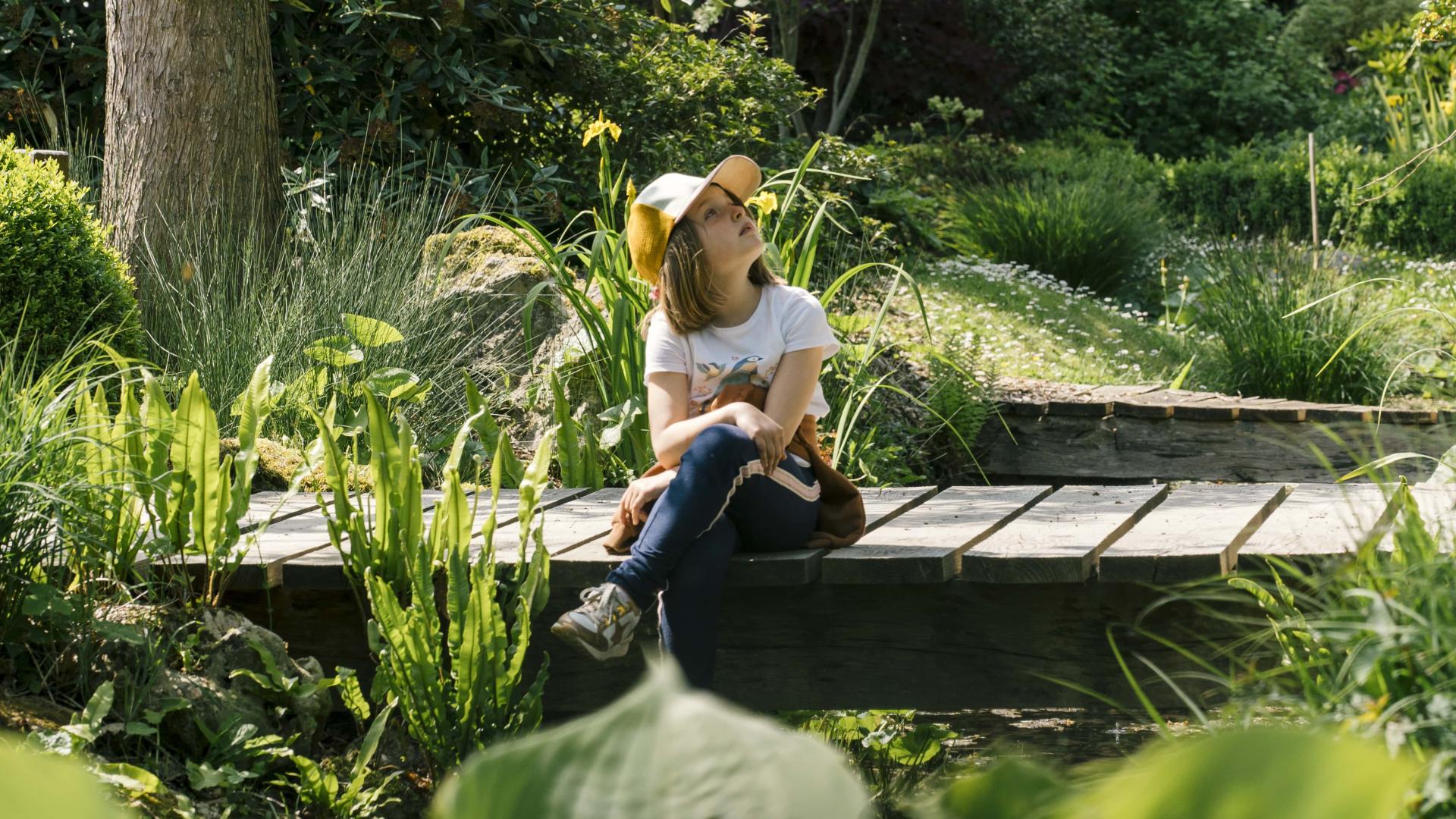 Une petite fille assise sur un pont au milieu d'un jardin verdoyant