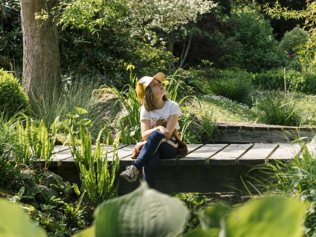 Une petite fille assise sur un pont au milieu d'un jardin verdoyant
