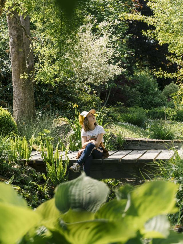 Une petite fille assise sur un pont au milieu d'un jardin verdoyant