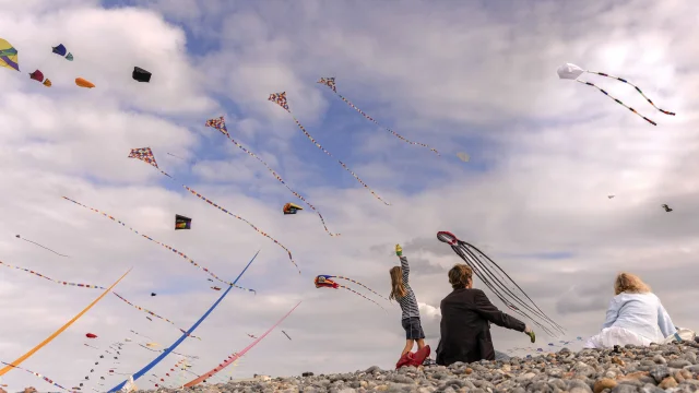 Une fille et sa grand-mère, assises à la plage, regardent des cerfs-volants.