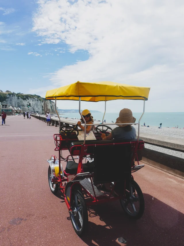 2 petites filles avec des chapeaux à bord d'une rosalie, voiturette à pédale, le long de l'esplanade de Dieppe, face aux falaises et à la mer