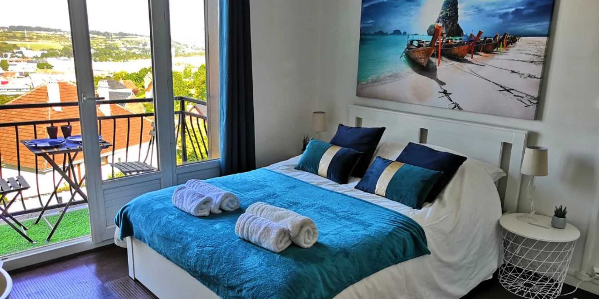 Le coin chambre d'un studio décoré dans les tons blancs, donnant sur un petit balcon avec une table