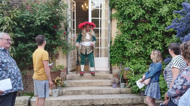 Un comédien en habit de l'époque de Louis XIV devant des participants au Cluedo