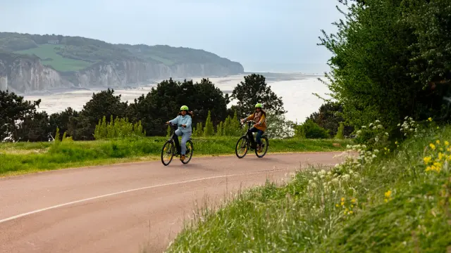 Couple à vélo en bord de mer à Pourville, longeant les falaises sous le soleil.