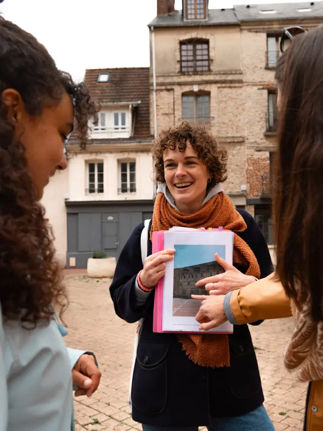 Une guide souriante montre une photo d’archive à deux participantes lors d’une visite commentée dans le centre historique de Dieppe.